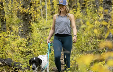 Woman hiking through woods with dog on leash