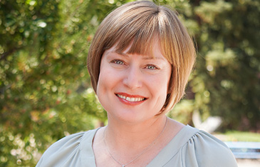 A photo of the new director for the Vail Public Library, Kim McNally. She is wearing a pale green dress in an outdoor setting.